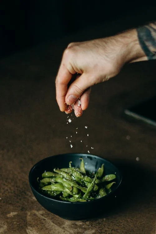 Green beans in a bowl, a hand sprinkling salt on top of it.