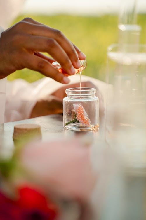 a woman's hand pouring a holiday essential oil to a jar with flower.