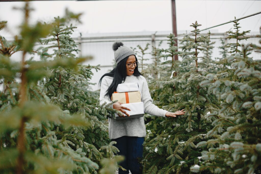 A girl holding gifts surrounded by Christmas tree. Thanksgiving gift ideas for employees