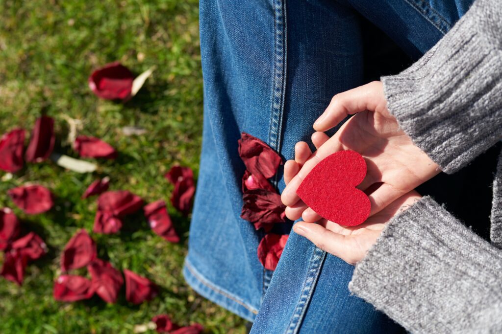 A woman with open palms holding a heart cut out decorating a Valentine's door ideas with flowers on the garden floor.