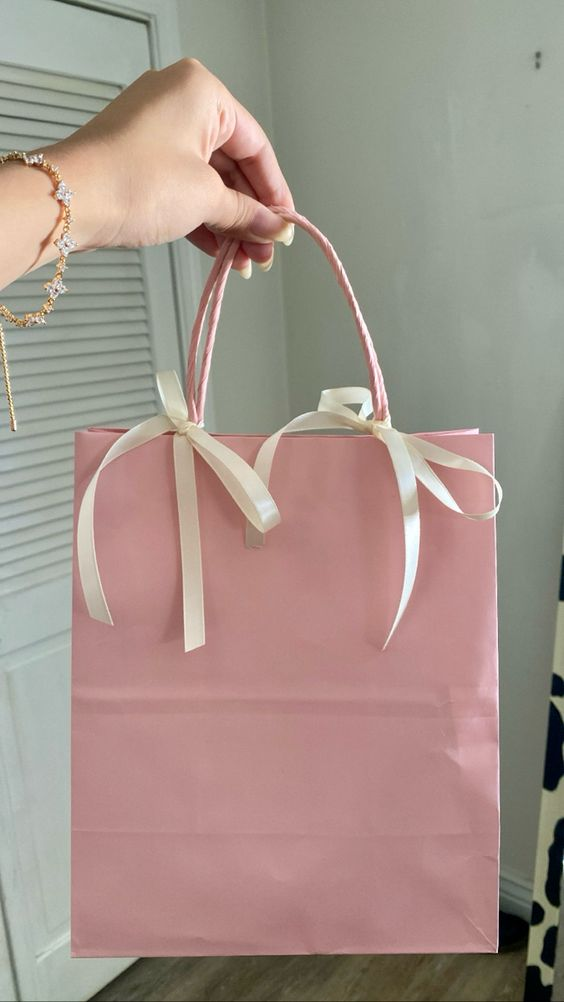 A coquette pink gift bag with white bow as a goodie bag for vision board party ideas.