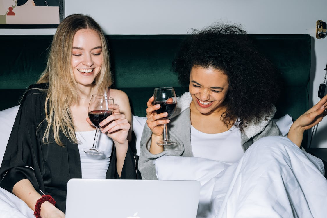 Two friends drinking wine while in a virtual meeting for a virtual vision board party ideas.