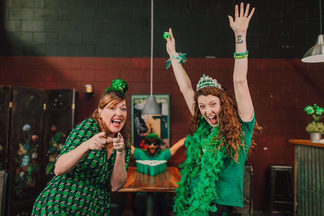 Two women having fun with their green dress and shirts to conclude a St Patrick's Day office ideas.