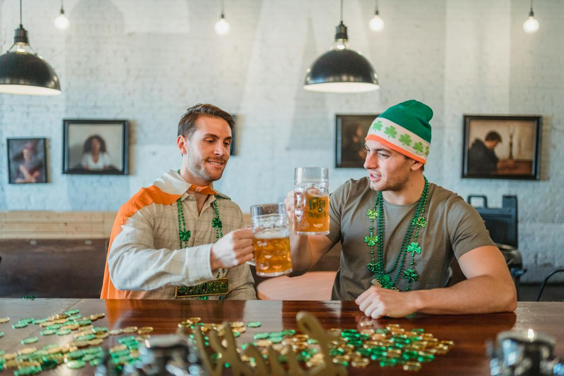 Two men clicking jars of beer with festive clover necklaces to celebrate St Patrick's Day office ideas