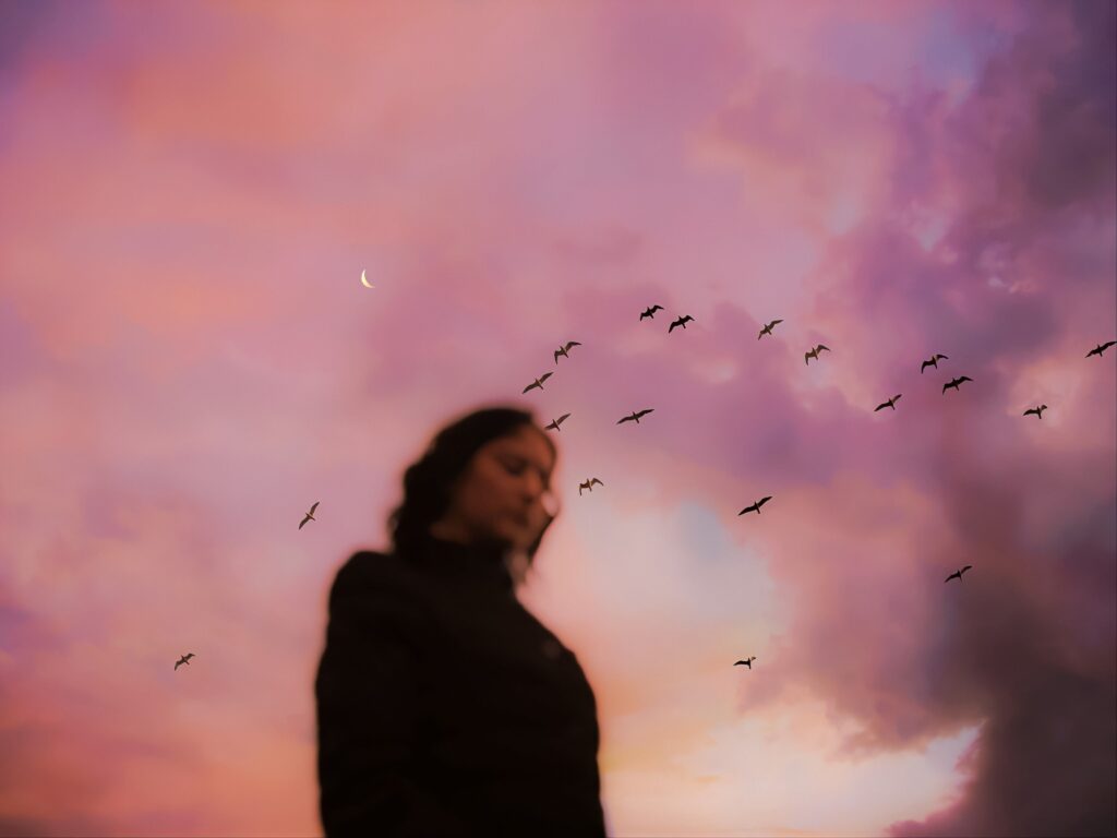 Woman towering in a pink skies background with birds flying a sign for a great Vision board party ideas.