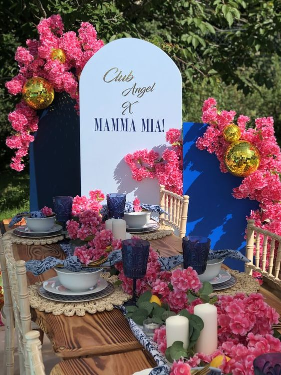 Mamma Mia party ideas for decor an arch blue panel with fuschia pink flowers and golden disco balls.